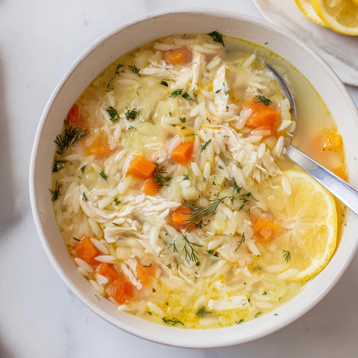 Creamy Greek Lemon Chicken Soup with Orzo, garnished with fresh dill and lemon slices.  
