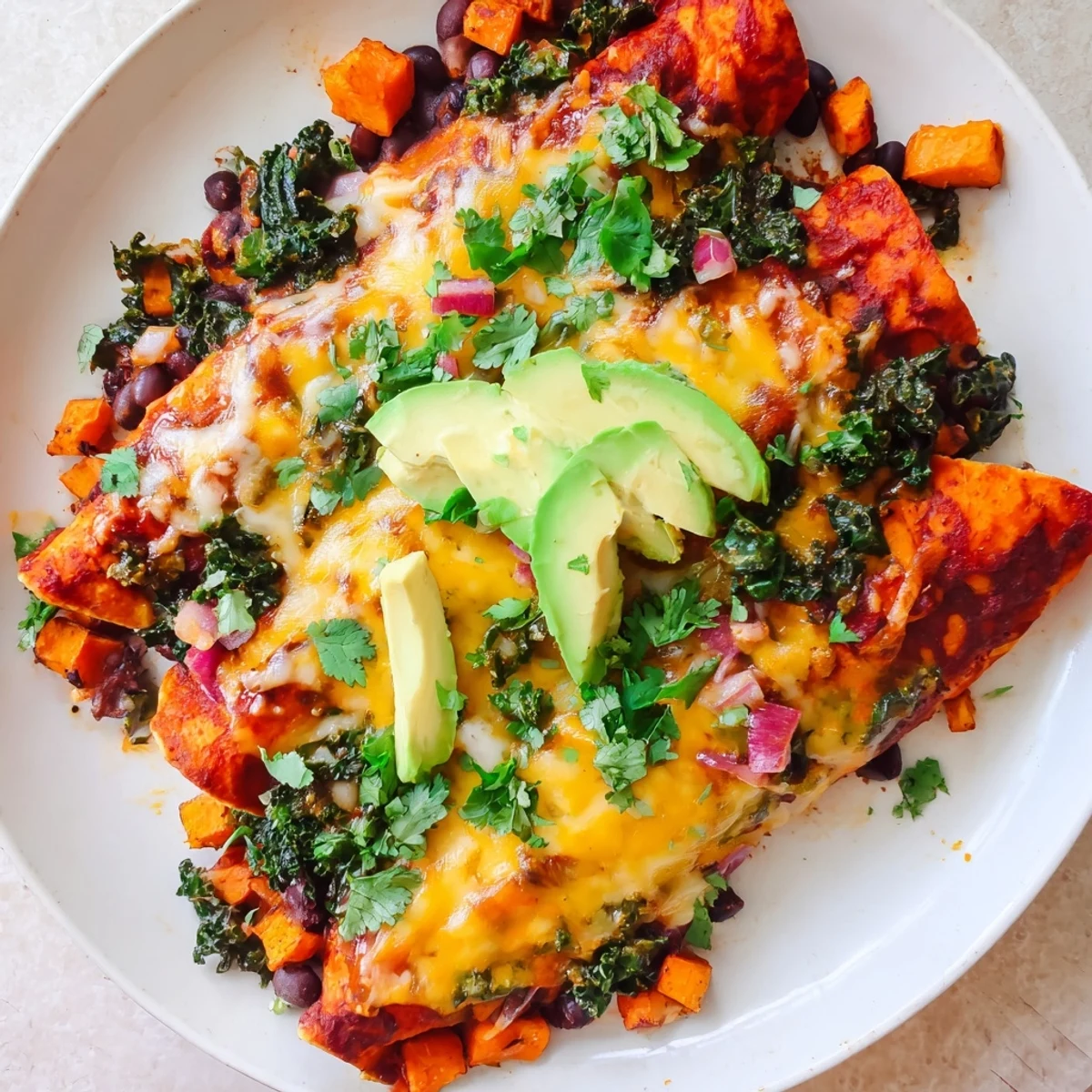 A single pan holds hearty one-pan sweet potato, black bean & kale enchiladas, topped with melted cheese and ready to enjoy.