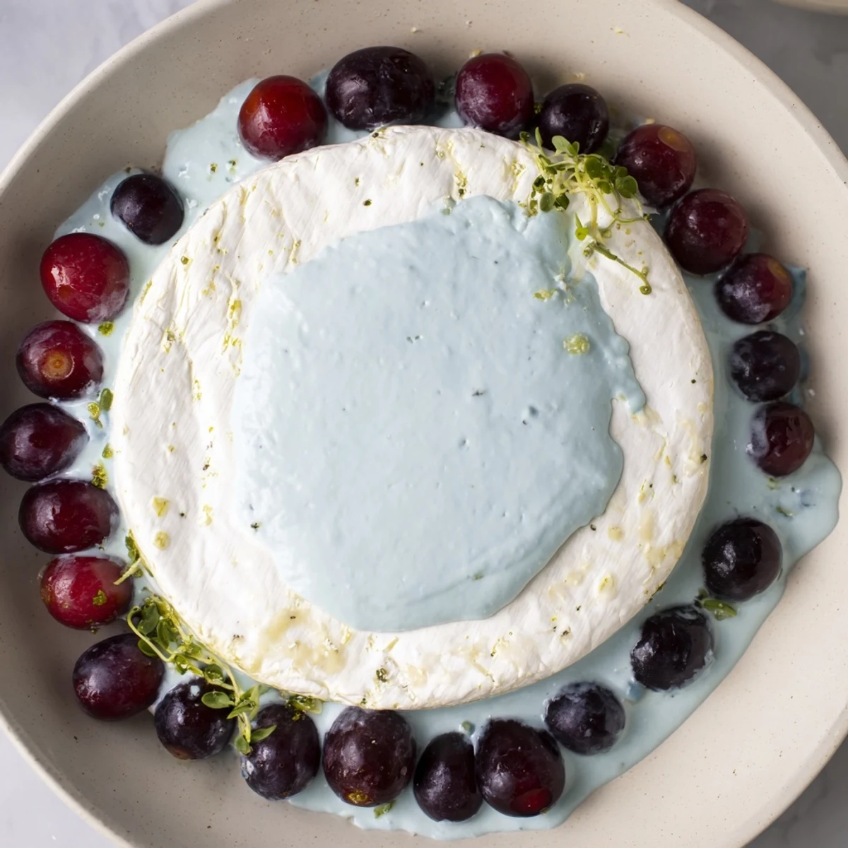Floating Island appetizer: a creamy Brie "island" surrounded by vibrant blue yogurt and dark grapes.