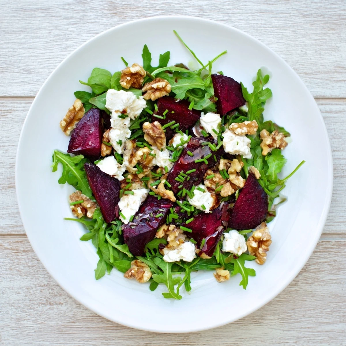 Vibrant roasted beet goat cheese salad with baby arugula, toasted walnuts, and a tangy balsamic vinaigrette on a white plate.  