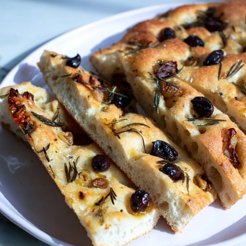 Golden Rustic Olive Oil Focaccia Bread topped with rosemary and black olives, ready to enjoy.  