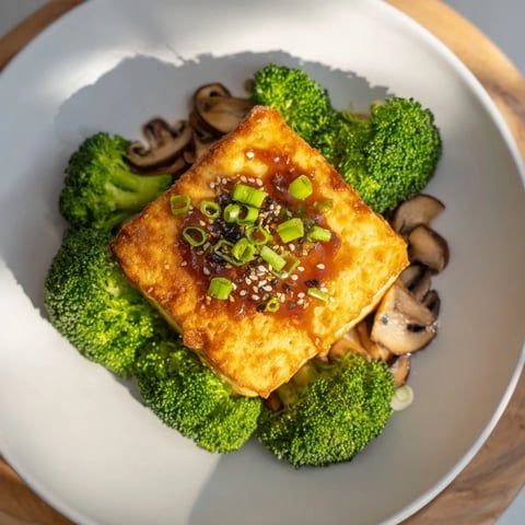 Golden-brown sautéed tofu steak rests alongside vibrant broccoli and shiitake mushrooms, ready to eat.