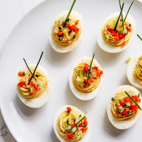 Festive deviled egg ornaments, brightly decorated with peppers and chives, ready to eat this holiday season.
