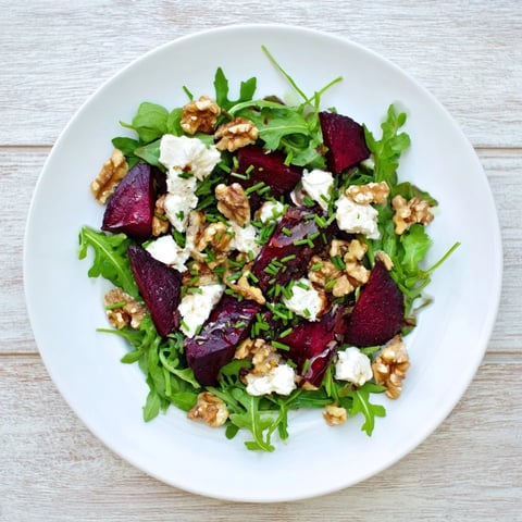 Vibrant roasted beet goat cheese salad with baby arugula, toasted walnuts, and a tangy balsamic vinaigrette on a white plate.  