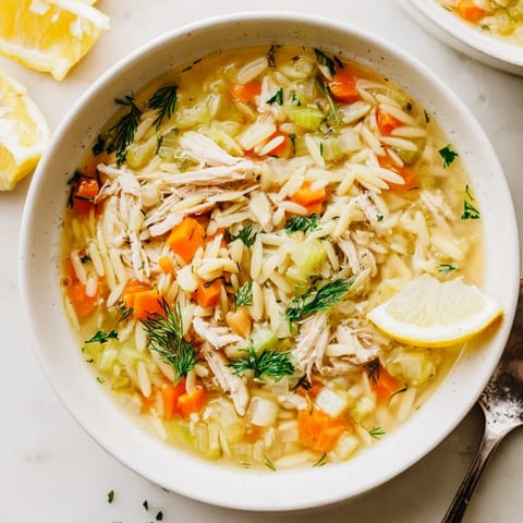 A steaming bowl of Greek Lemon Chicken Soup with Orzo, showcasing vibrant vegetables.  