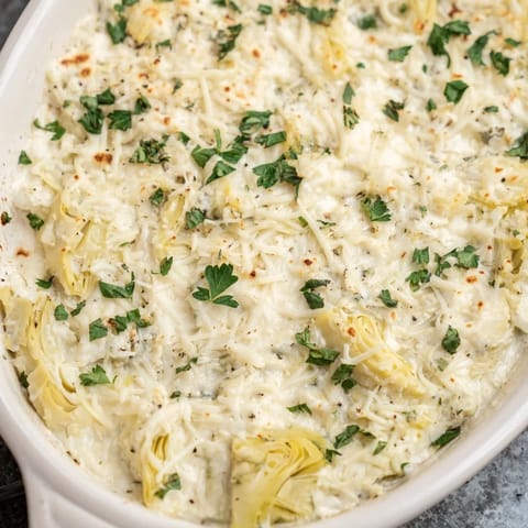 A close-up of creamy, cheesy baked artichoke dip, perfect served with crackers and fresh parsley garnish.