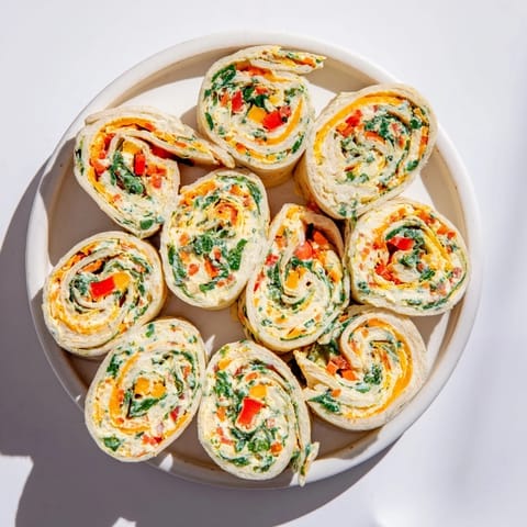 These Cozy Scarf Holiday Pinwheel Wraps feature a vibrant mix of fresh veggies rolled in a tortilla.