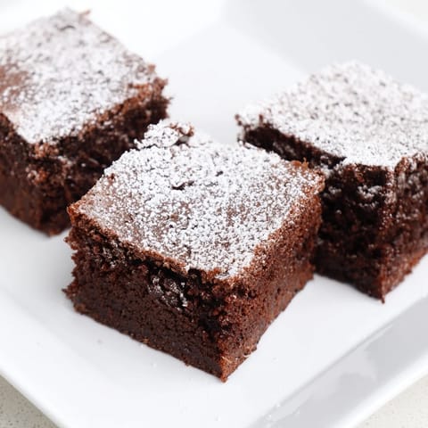 Warm, freshly baked brownie squares with a light dusting of powdered sugar served on a plate.