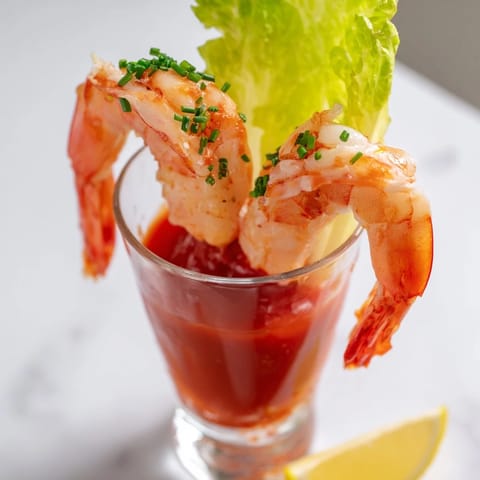 These vibrant retro prawn cocktail shooters feature chilled prawns atop a spicy, flavorful cocktail sauce.