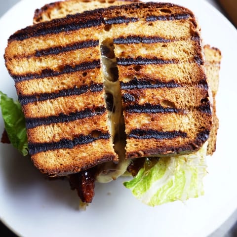Vegan Bacon BLT Grilled Cheese on a plate, featuring crispy tempeh bacon, juicy tomato, and crisp lettuce between buttery bread.