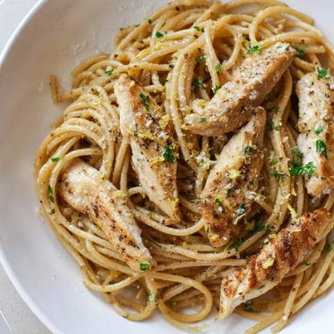 A close-up of seared chicken strips over lemony brown butter pasta, garnished with grated Parmesan.