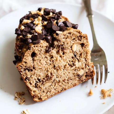 A close-up of Chocolate Chip Peanut Butter Oatmeal Banana Bread shows a tender crumb studded with chocolate chips and chopped roasted peanuts.