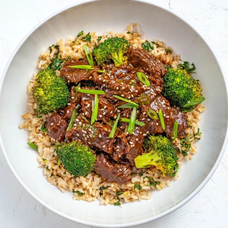 Close-up of slow-cooker beef & broccoli showing the rich, glistening sauce and fluffy brown rice below.