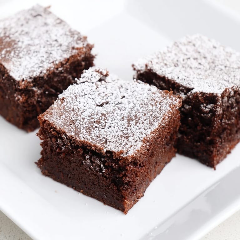 Warm, freshly baked brownie squares with a light dusting of powdered sugar served on a plate.