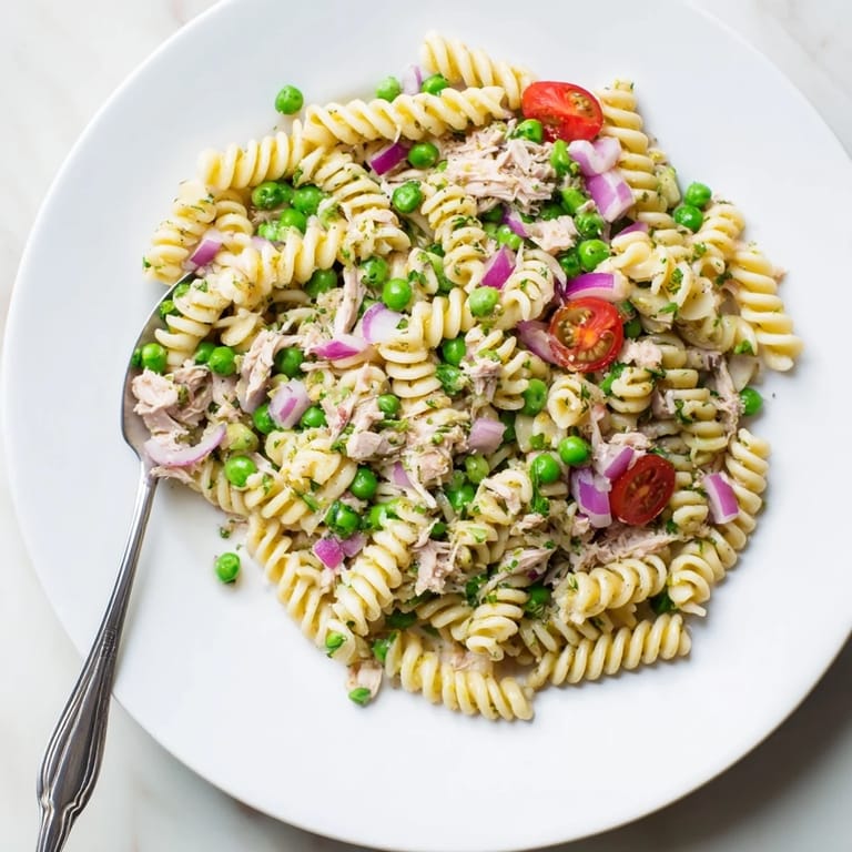 A close-up of Lemony Tuna Pasta Salad highlights juicy cherry tomatoes and briny capers nestled among the pasta and tender tuna flakes.