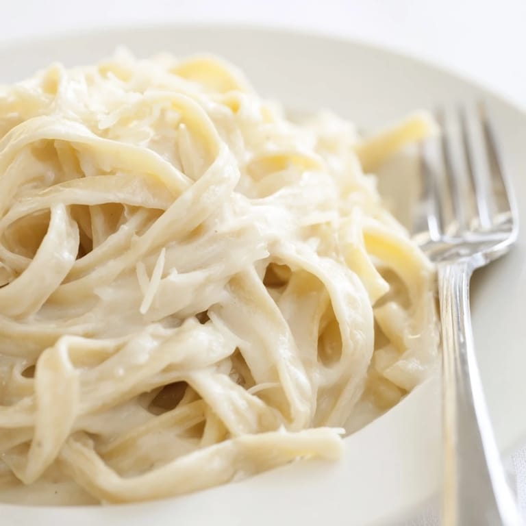 Steam rises from a plate of Easy Creamy Cauliflower Alfredo, highlighting the smooth sauce clinging to al dente pasta strands.
