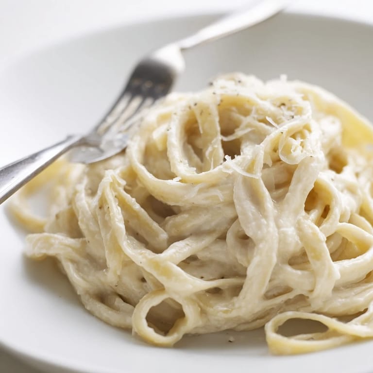 Close-up of Easy Creamy Cauliflower Alfredo showing a rich, creamy sauce with flecks of black pepper and fresh parsley.