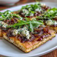 Crispy flatbread pizza with sweet caramelized onions, creamy mozzarella, tangy goat cheese, and peppery arugula—drizzled with balsamic glaze for gourmet flavor.