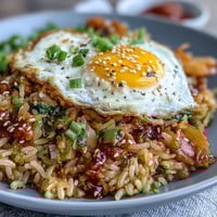 Kimchi cabbage fried rice with a sunny-side-up egg, vibrant vegetables, and sesame seeds for crunch.  